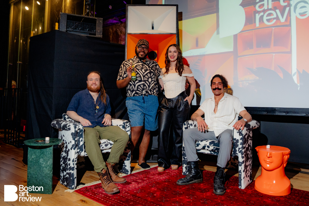 Luke McCarthy and Stephen Rosenberg of Sound Logic Boston, Sheldon Gray of Dive Bar Caviar, and Kristen Bender-Daaboul, Founder of Kadeema Rentals, seated in front of the Boston Art Review projection with Kadeema’s Floria Cowhide Pattern Velvet Chairs, Angled Green Marble Table, David Orange Bust Table, and red area rug.
