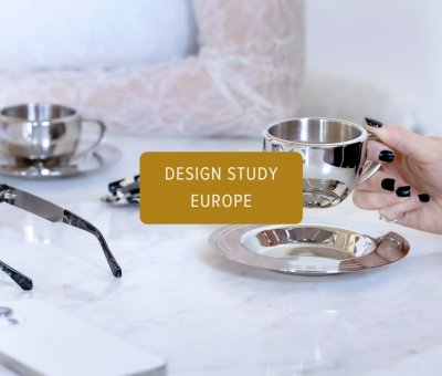 Hand holding a silver espresso cup beside sunglasses and a phone during a quiet creative reflection moment.
