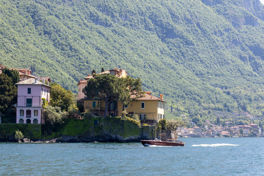 Lake Como shoreline with colorful villas, forested mountains and a boat on the water in Italy
