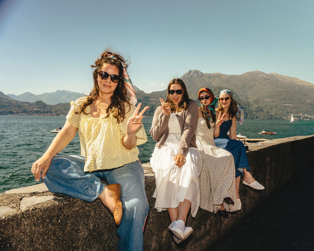 Four women sitting by Lake Como with mountains and water in the background, Italy
